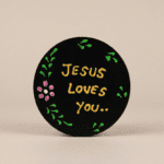 “Black round magnet with floral accents reading ‘Jesus loves you’ on a stainless steel refrigerator.”