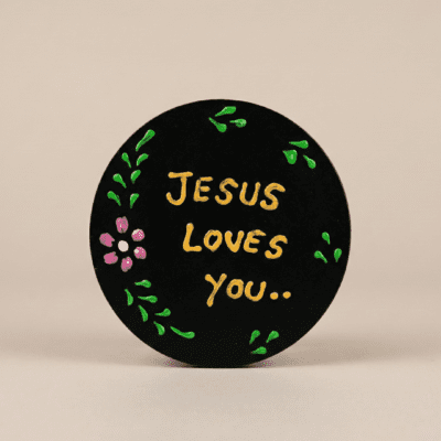 “Black round magnet with floral accents reading ‘Jesus loves you’ on a stainless steel refrigerator.”