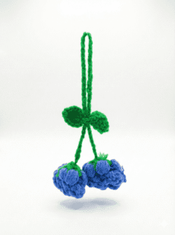 Handmade crochet blue cherry charm with green stems and loop held in hand, made from yarn
