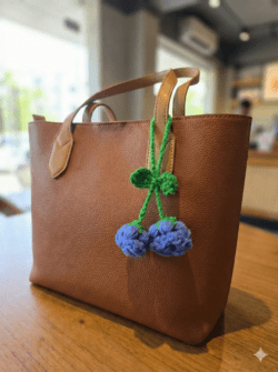 Handmade crochet blue cherry charm with green stems and loop held in hand, made from yarn