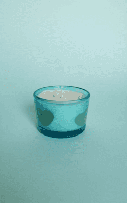 “Blue frosted glass candle with cream wax and embedded heart-shaped wax designs”