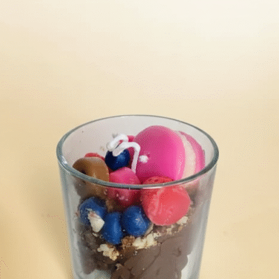 Dessert-style wax candle in a glass jar with pink macaron, blueberries, raspberries, chocolate wax and cookie crumble