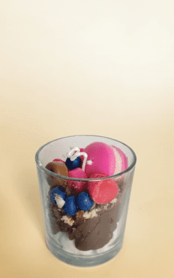Dessert-style wax candle in a glass jar with pink macaron, blueberries, raspberries, chocolate wax and cookie crumble