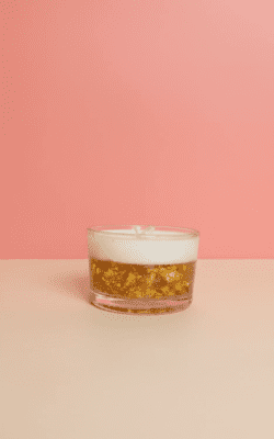 “Luxury gel and cream wax candle in a low glass cup with floating gold flakes”