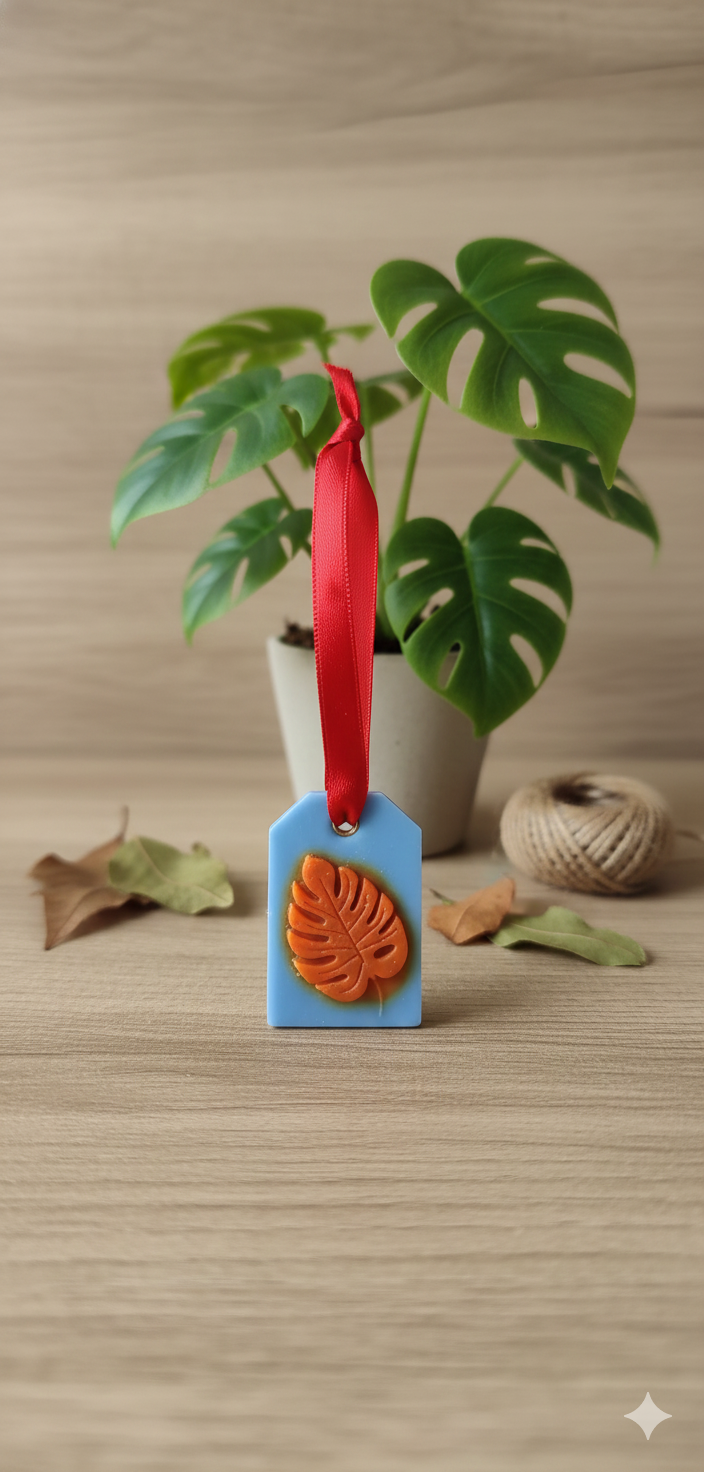 “Hanging wax room freshener with blue base, orange leaf emboss and red ribbon”