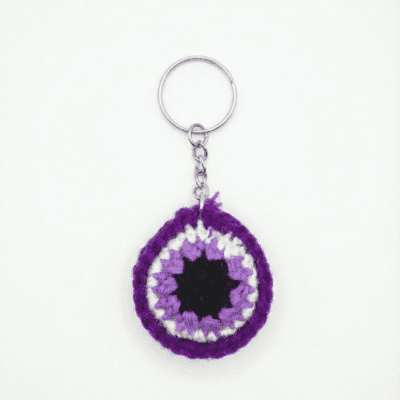 Handmade purple crochet round keychain with floral-style centre attached to a metal keyring