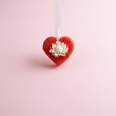 Heart-shaped red wax room freshener with white floral center and gold shimmer, hanging on white ribbon