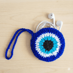 Handmade crochet evil eye charm in blue and white yarn with hanging loop on wooden background