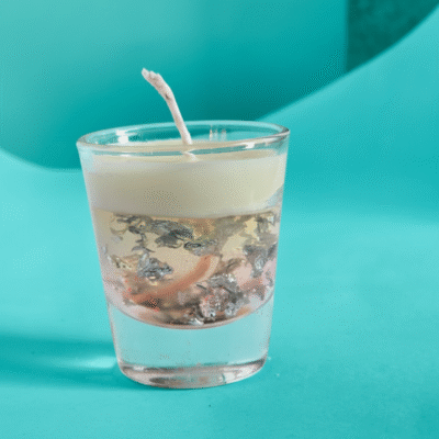 “Transparent gel and cream wax scented candle with floating silver flakes in a glass cup”