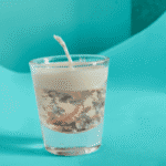 “Transparent gel and cream wax scented candle with floating silver flakes in a glass cup”