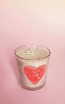 “White scented wax candle in glass cup with embedded red heart and golden flakes”