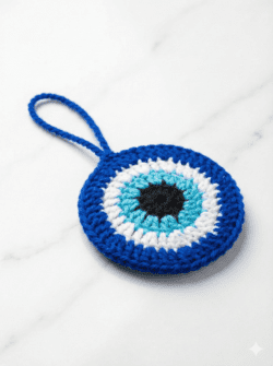 Handmade crochet evil eye charm in blue and white yarn with hanging loop on wooden background