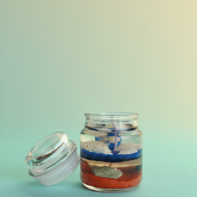 Ocean-themed blue gel wax candle with embedded seashells and cream wax layer in a glass jar