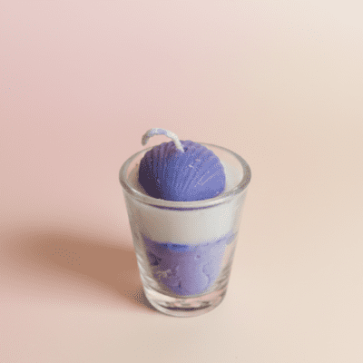 Handcrafted pastel layered seashell candle placed in a transparent glass shot jar on a white background