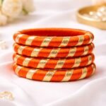 Orange silk thread bangles with gold diagonal metallic stripes stacked on a white fabric background