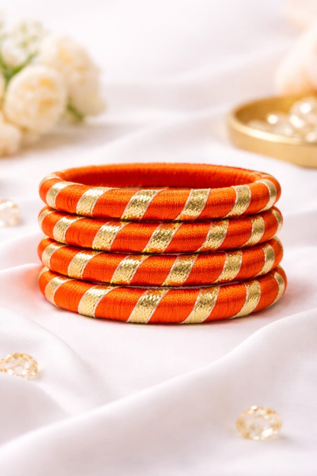 Orange silk thread bangles with gold diagonal metallic stripes stacked on a white fabric background