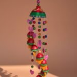 “Vibrant handcrafted terracotta wind chime with colourful bells and beads hanging in sunlight”