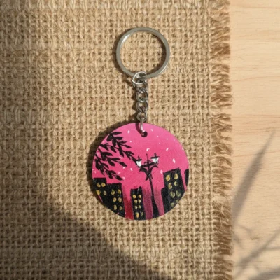 Handmade pink cityscape MDF round keychain with street lamp and building design on textured background