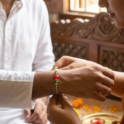 Handmade designer beaded Rakhi with blue and yellow braided thread and decorative red and green beads for Raksha Bandhan.