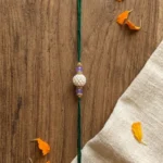 Handmade white pearl Rakhi with lavender stone beads and green thread for Raksha Bandhan celebration.