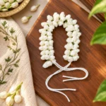 Handmade white crochet jasmine flower gajra hair braid with tie-back cords on a wooden board with fresh jasmine buds