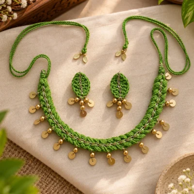 Handmade green crochet necklace with gold coin drops and matching leaf-shaped earrings on beige linen fabric